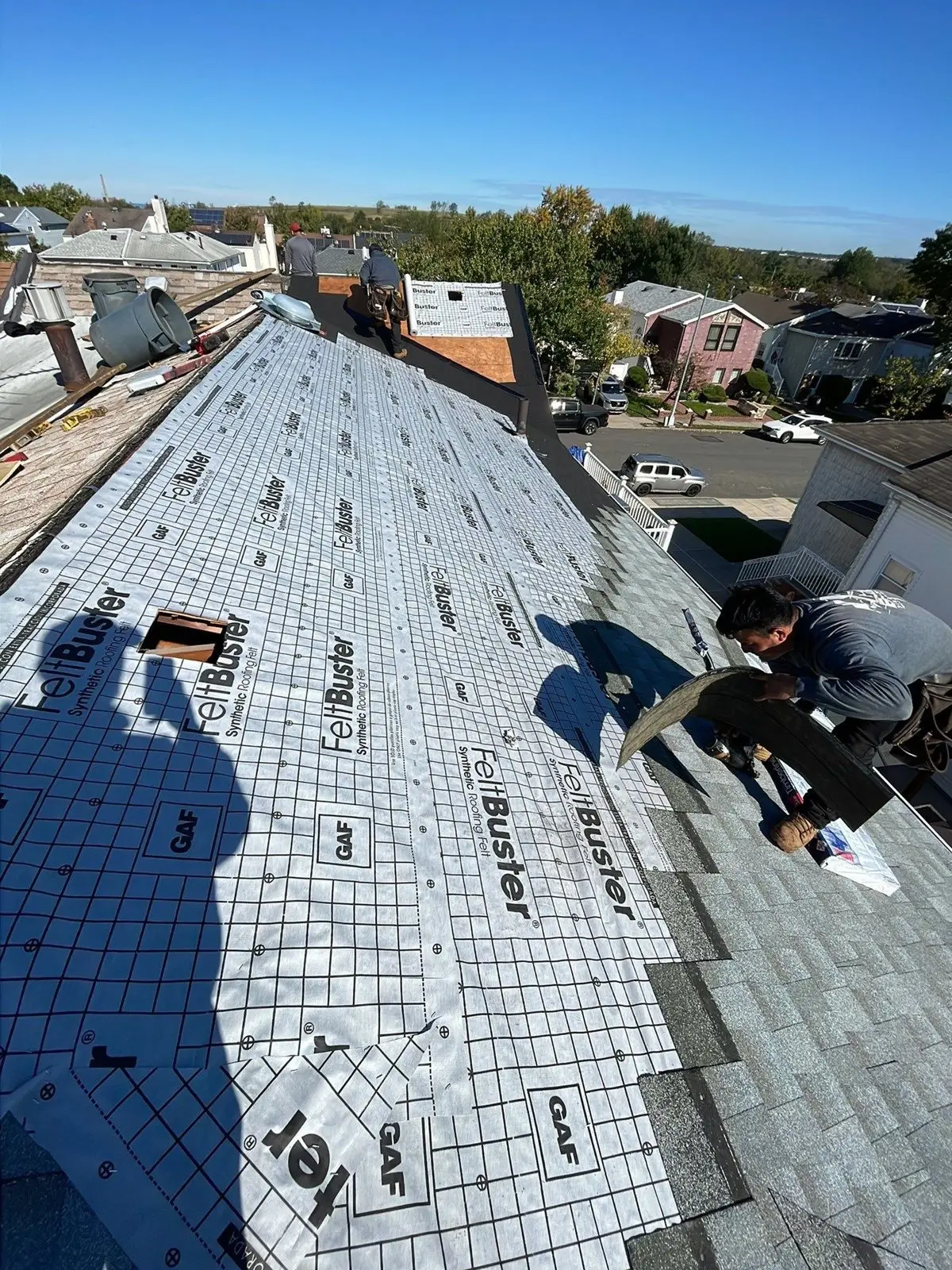 Roofers installing synthetic underlayment over new roof sheathing