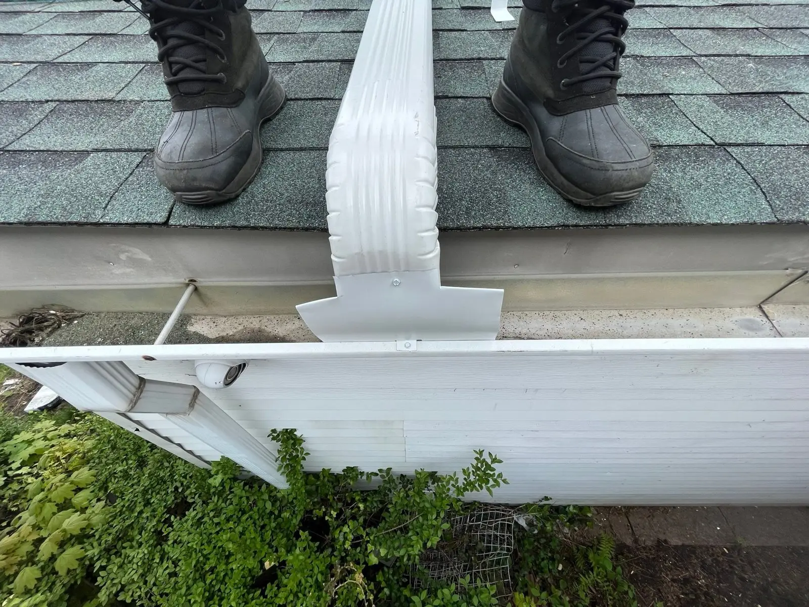 New white seamless gutter and downspout outlet on a Staten Island roof edge