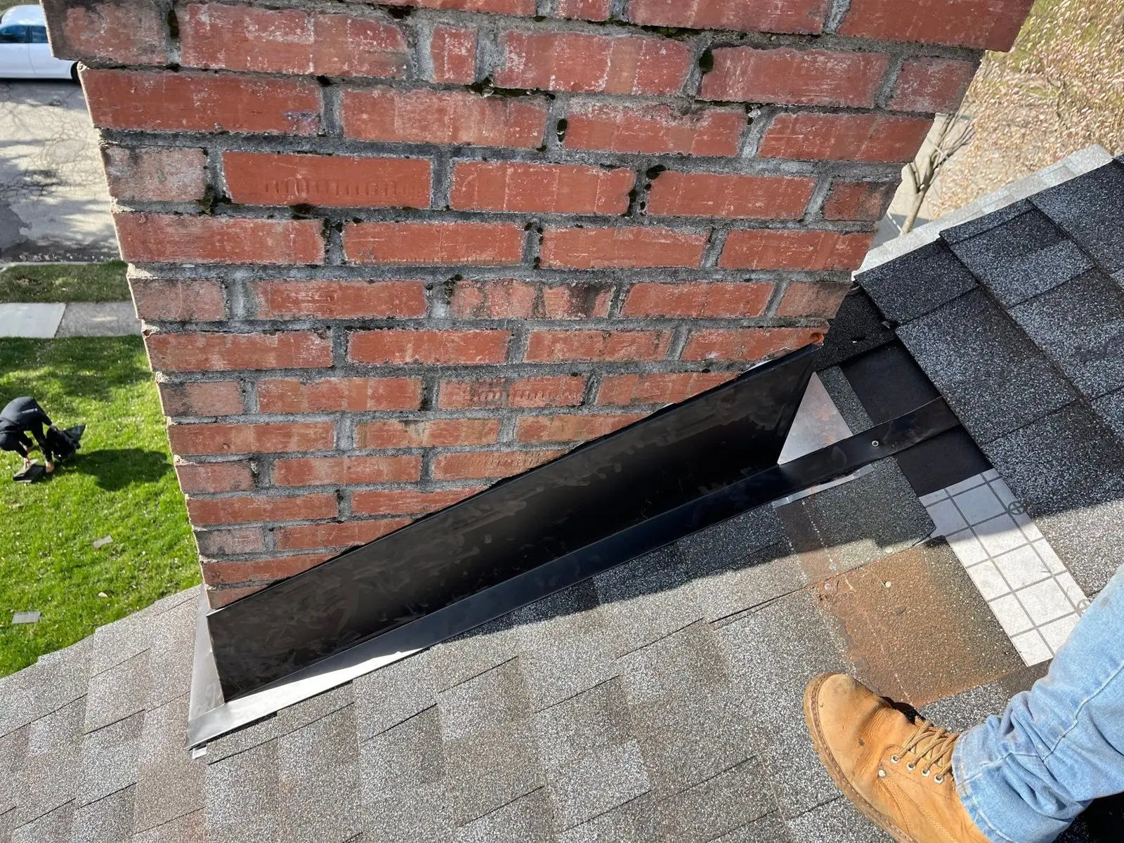 New step and counter flashing along a brick chimney on a shingle roof