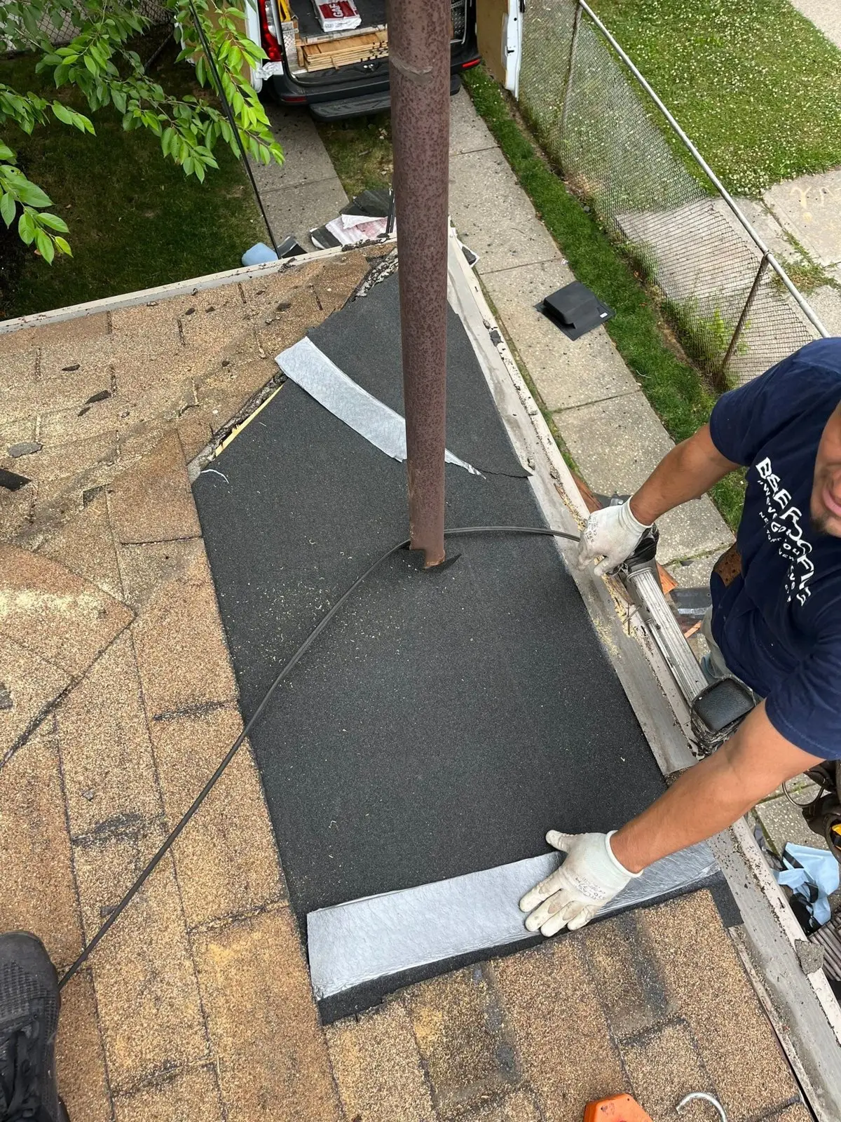 Roofer installing new underlayment and metal flashing around a vent pipe